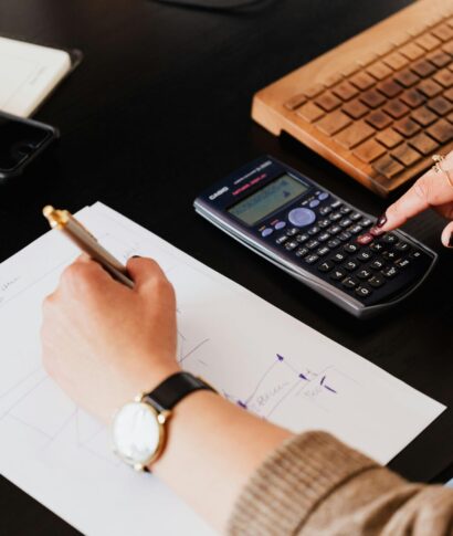 pexels-photo-4476375-4476375 Close-up of hands working with a calculator and notebook on a desk, analyzing documents.