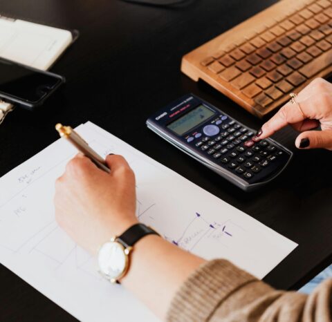 Close-up of hands working with a calculator and notebook on a desk, analyzing documents.